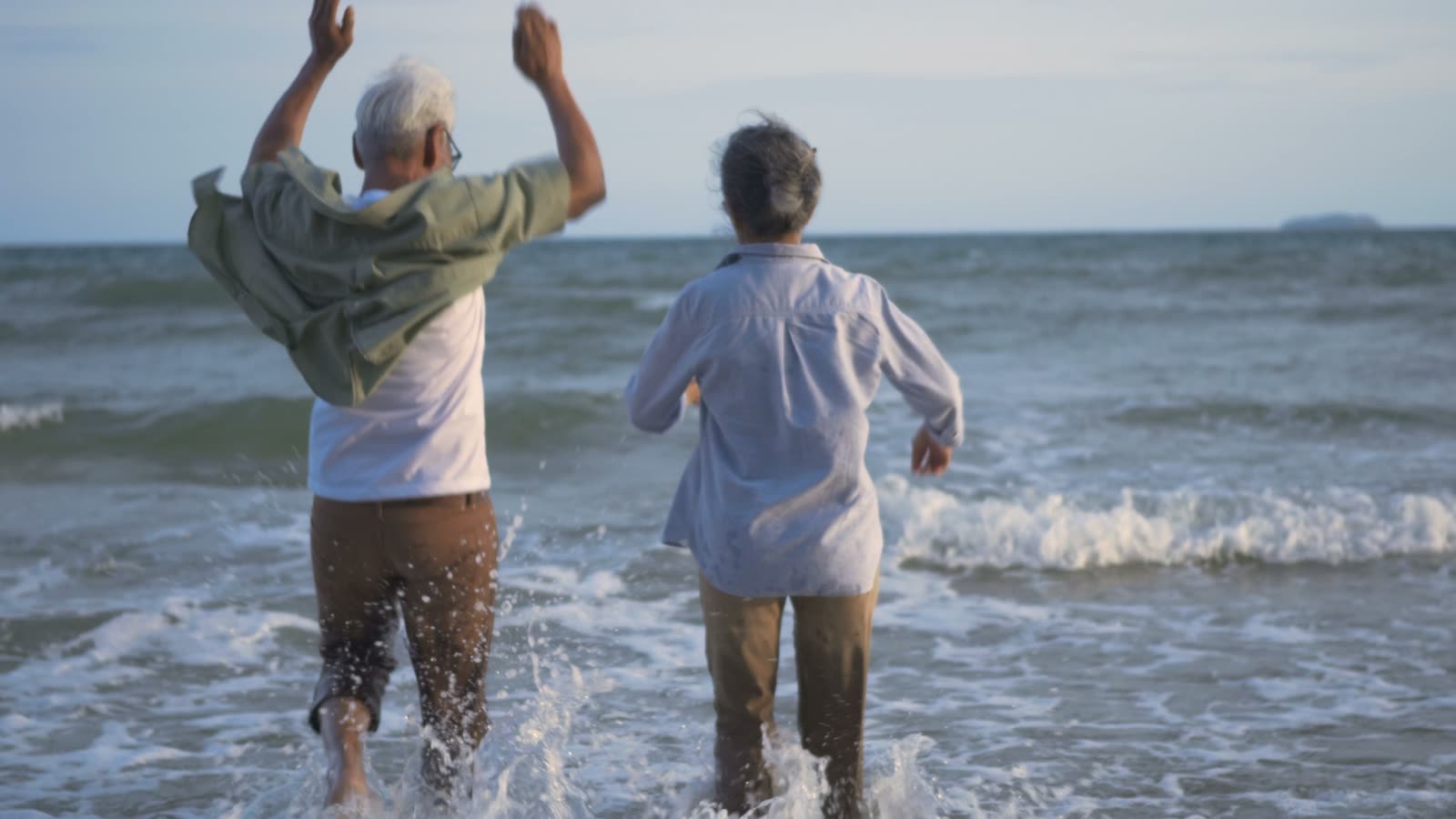 An older couple running into the sea, arms raised