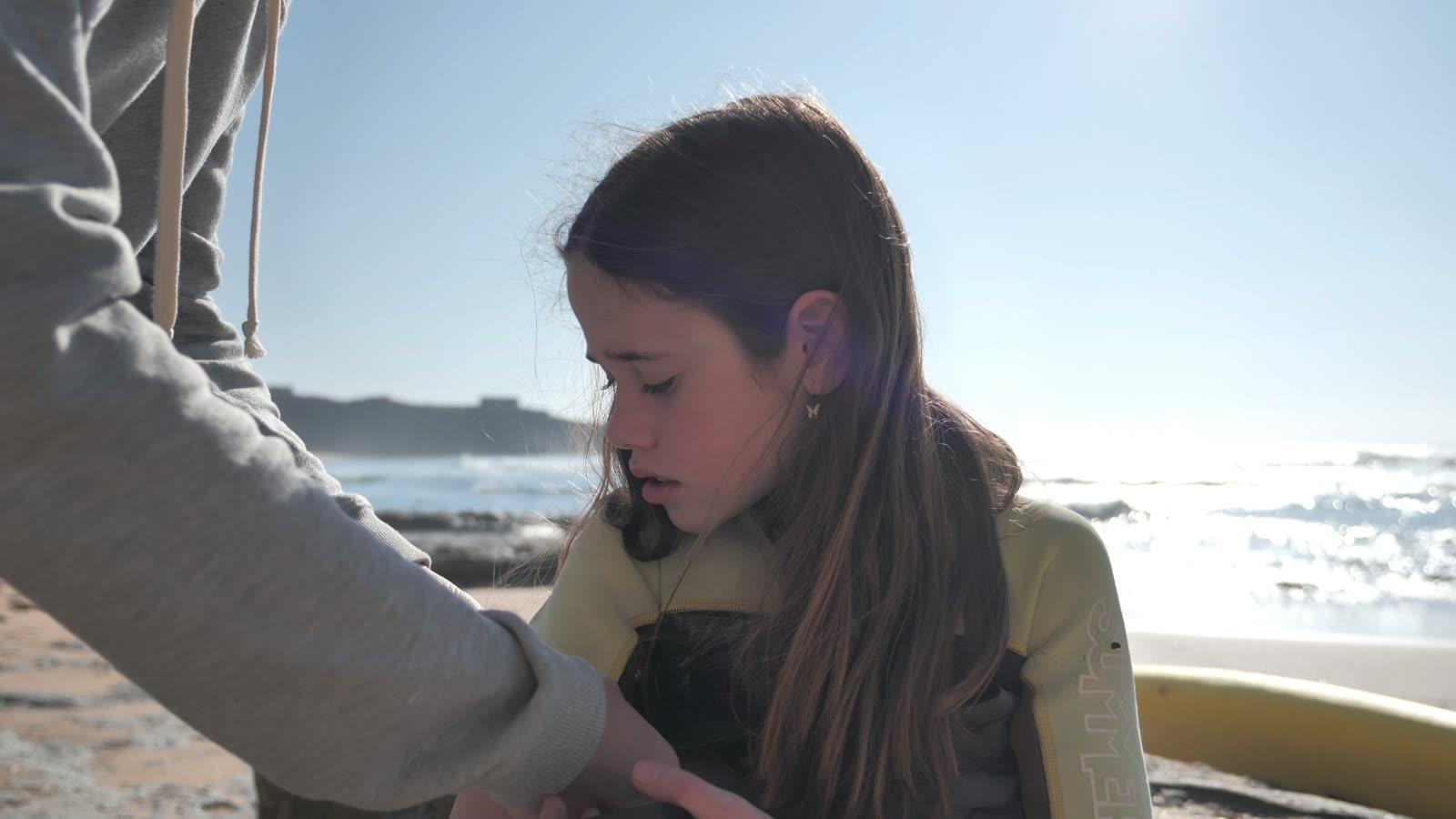 Young woman zipping up a wetsuit on the beach